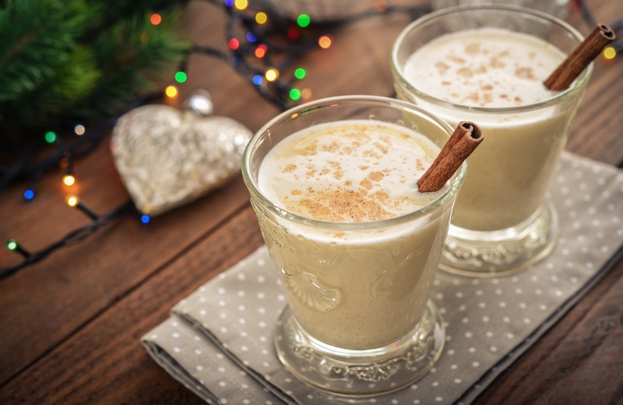 Traditional christmas drink eggnog in glass with spices and christmas lights on wooden background