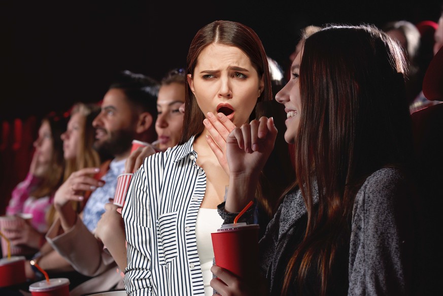 Group of female friends laughing and smiling watching a film together at the movie theatre snacks popcorn entertainment people lifestyle leisure friendship concept.