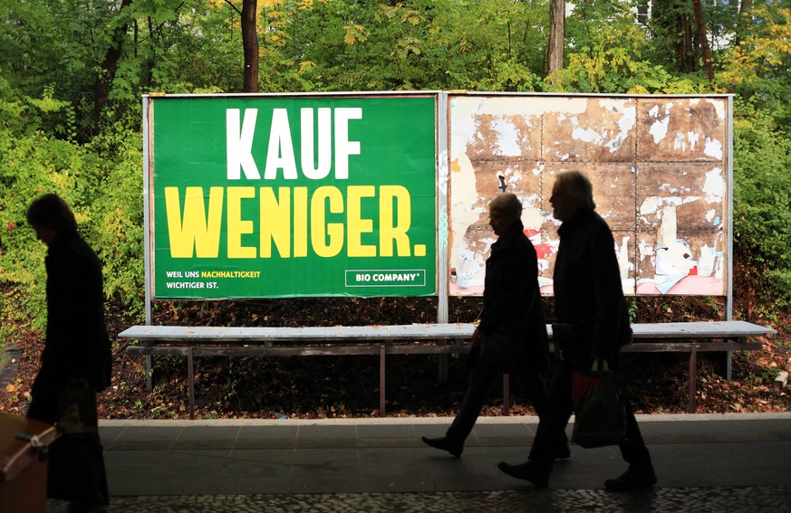 27.09.2019, Berlin. Leute gehen in Lichterfelde an der S-Bahnstation Botanischer Garten vor einem Großplakat der Bio Company mit der Aufschrift &quot;Kauf weniger.&quot; vorbei. Weniger Konsum, Luxusv ...