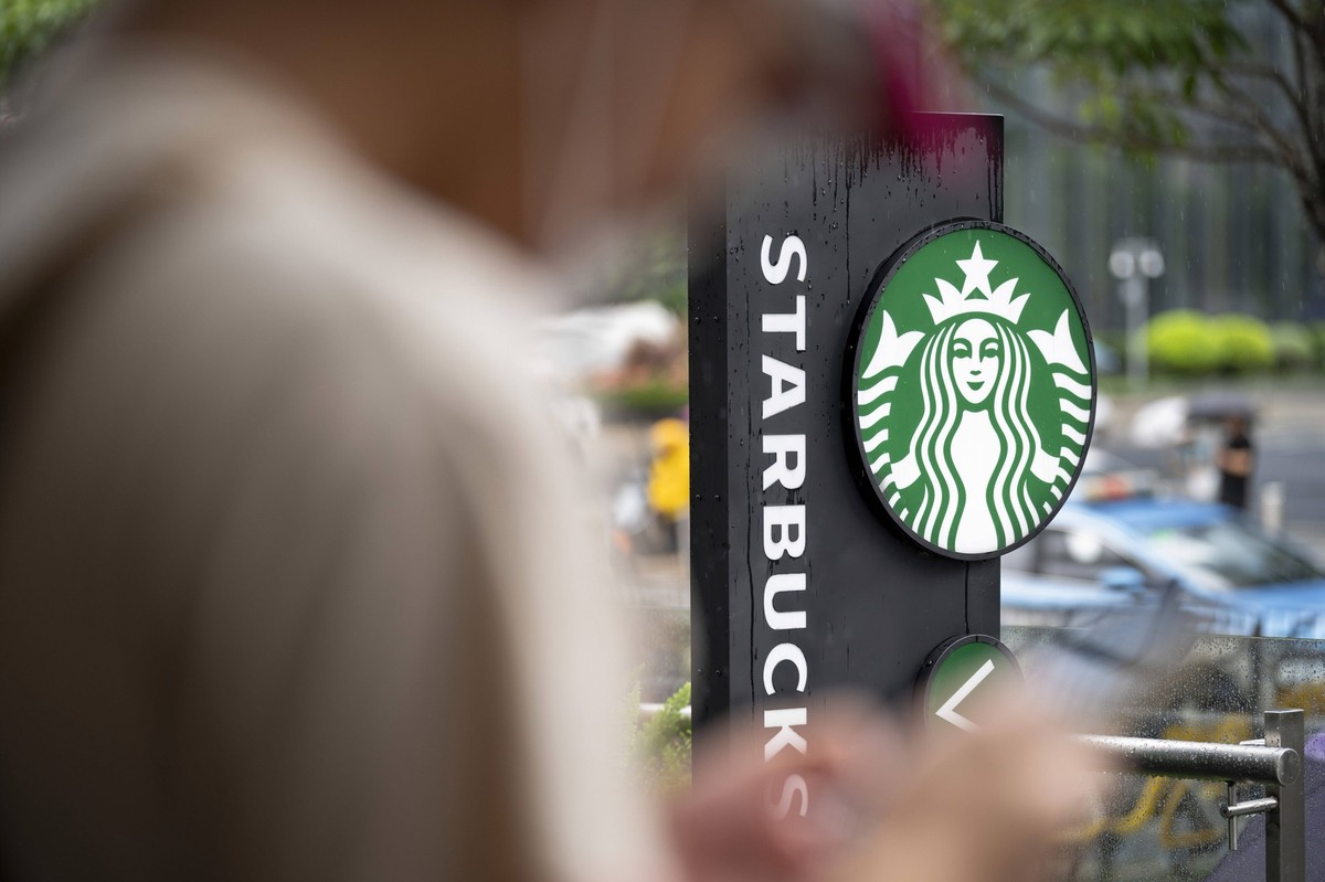Brands and Logos in Shenzhen, China - 8 Mar 2025 A man uses his phone as the American multinational chain Starbucks Coffee logo and store is seen in the backtround in Shenzhen, China. China Copyright: ...