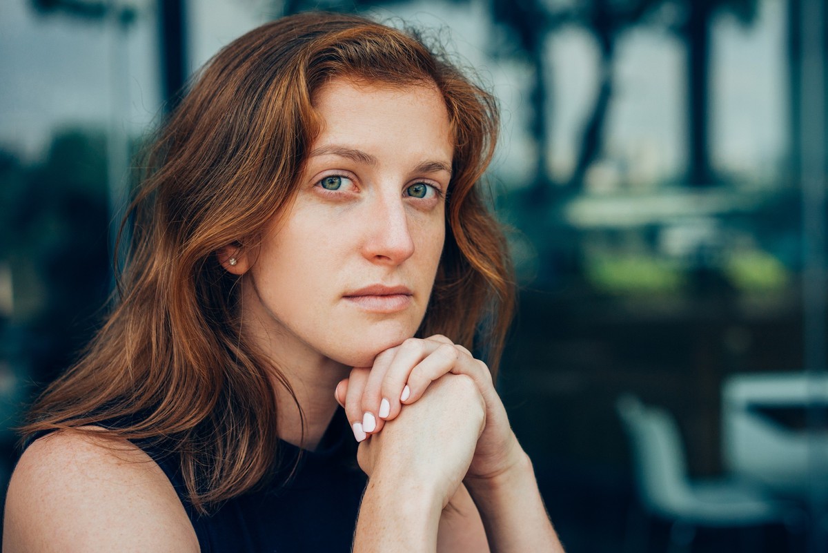 Closeup of serious young woman sitting at office cafe resting chin on hands. Young female manager thinking over great challenge. Business and challenge concept
