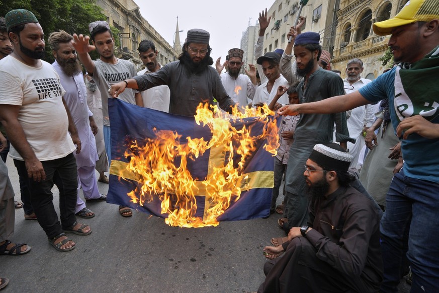 07.07.2023, Pakistan, Karachi: Anhänger der radikalen islamistischen Partei «Tehreek-e-Labaik Pakistan» verbrennen die schwedische Flagge während eines Protests gegen eine Koranverbrennung in Schweden ...