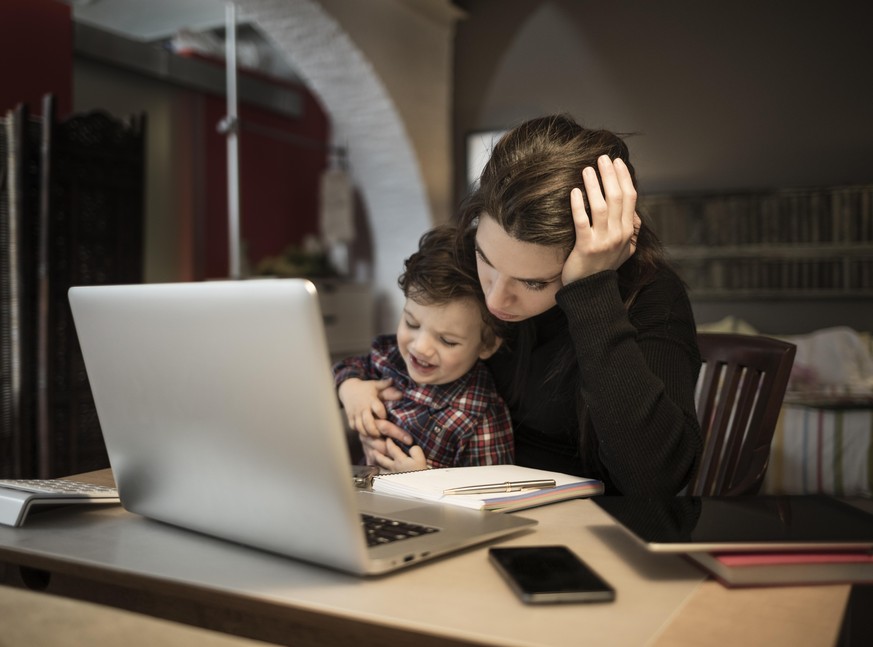 Worried woman working at home and holding her crying little son