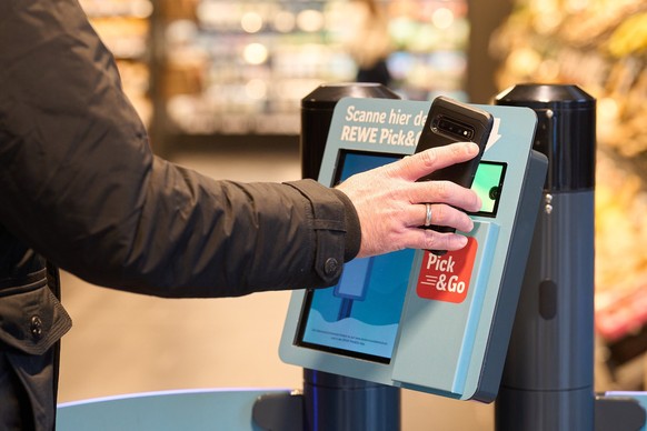 Der neue Supermarkt Rewe Pick&amp;Go in München ist zwar kassenlos, dafür müssen Kund:innen an einem Scan-Gerät vorbei. Rund um die Uhr geöffnet ist der Markt dadurch allerdings nicht. Es gelten die ü ...