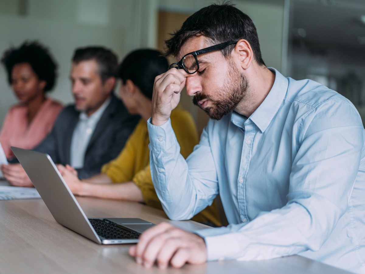 Overworked businessman sitting in the board room and holding head with hand while his colleagues discussing business strategy.
