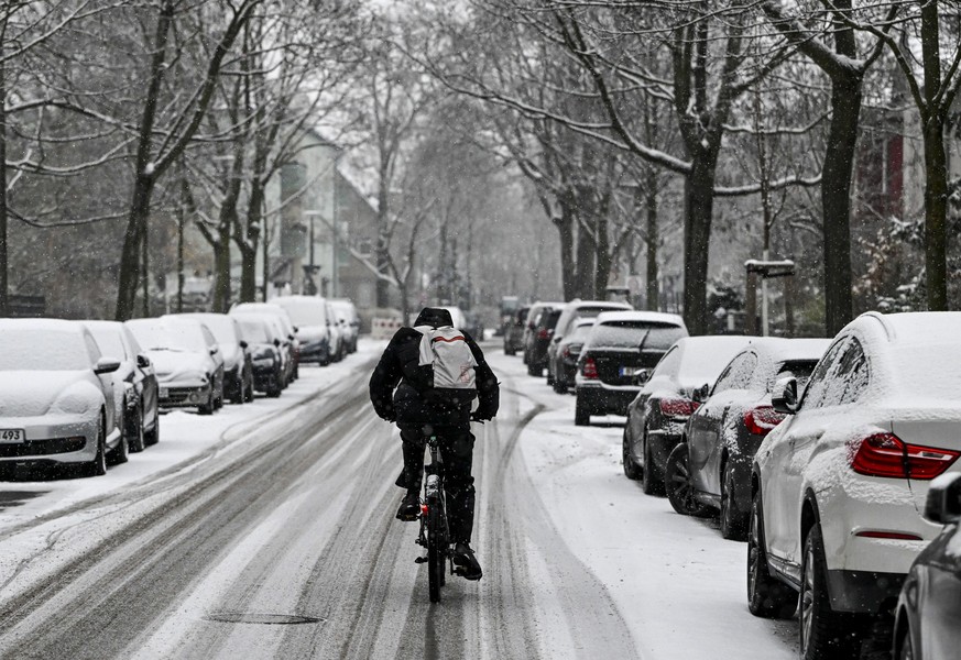 06.12.2023, Berlin: Ein Radfahrer fährt auf einer mit Schnee bedeckten Straße in Karlshorst, auf der die Spuren von Autos zu sehen sind. Durch Schneeregen und Schneeschauer bei nasskaltem Winterwetter ...