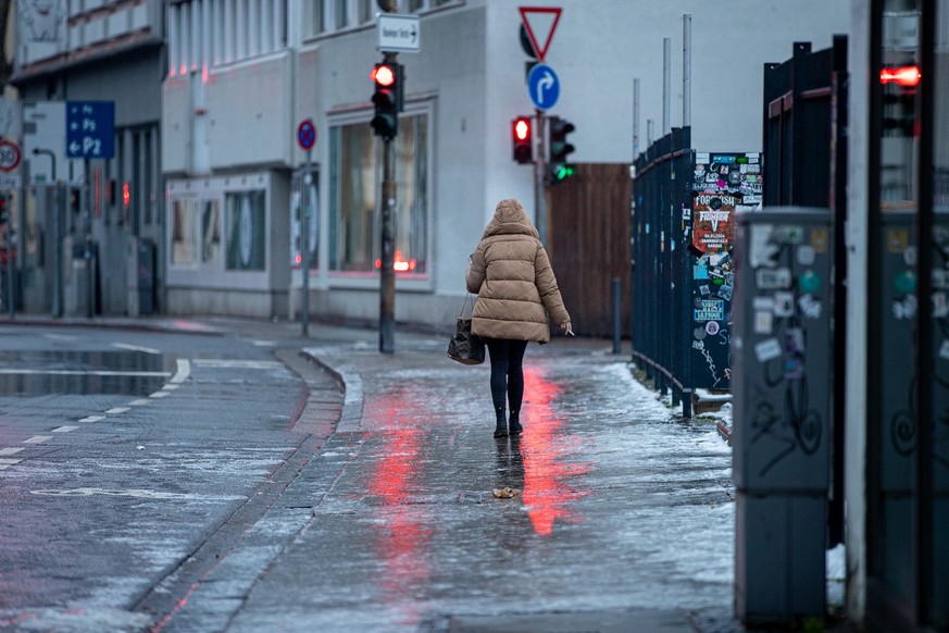 17.01.2024, Saarland, Saarbrücken: Eine Fußgängerin passiert einen Gehweg, der sich nach Blitzeis in eine Rutschbahn verwandelt hat. Eisregen hat für spiegelglatte Böden gesorgt. Foto: Laszlo Pinter/d ...