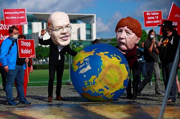 Demonstrators wearing masks depicting German Minister of Economic Affairs and Energy Peter Altmaier and Chancellor Angela Merkel hold an earth globe as activists protest for a faster coal exit in fron ...