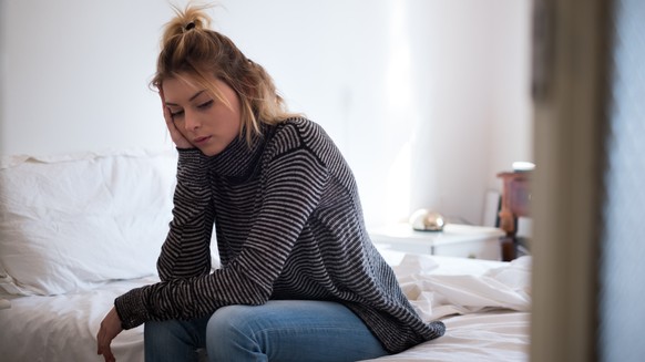 Sad young victim woman sitting on the bed at home suffering depression