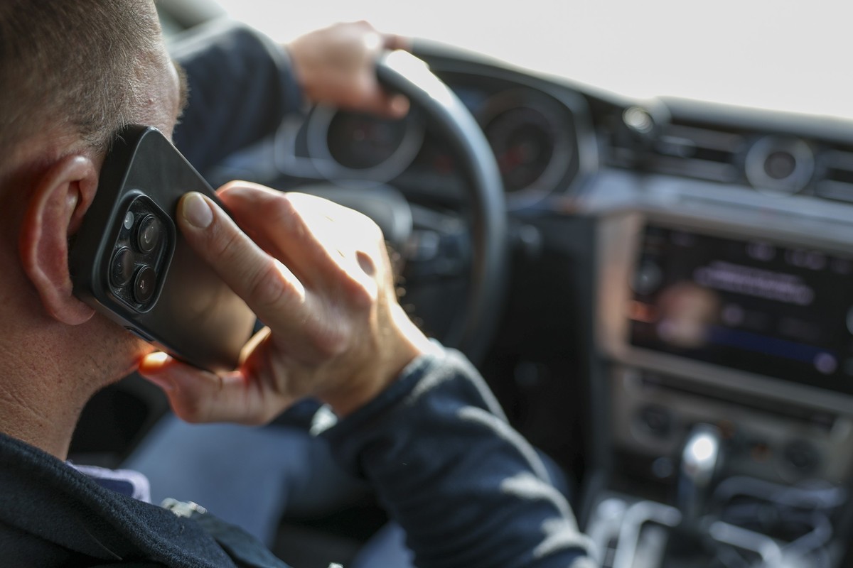 02.10.2025, Sachsen, Grimma: +++ Illustration +++ Ein Mann telefoniert in seinem Auto mit einem Smartphone. Das Unfallrisiko durch Ablenkung im Straßenverkehr steht im Fokus einer europaweiten Roadpol ...