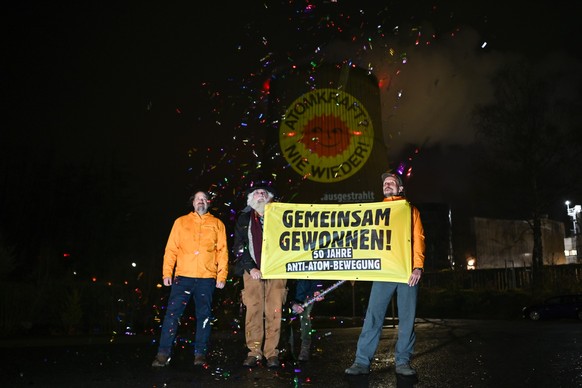 10.04.2023, Niedersachsen, Lingen: Aktivisten der Anti-Atom-Bewegung halten ein Banner und schießen Konfetti in die Luft, während sie eine große Anti-Atom-Sonne auf den Kühlturm des Atomkraftwerkes Em ...