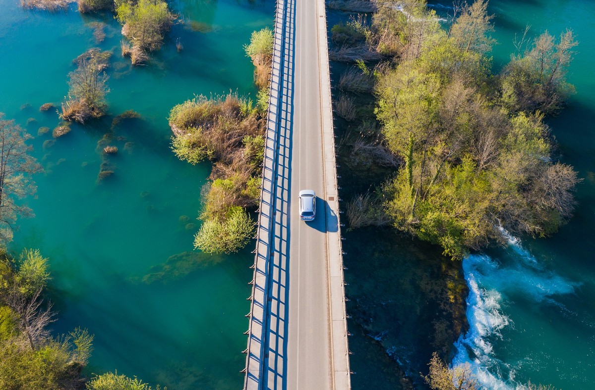 Car crossing bridge over Mreznica river in Belavici village from drone, waterfalls and trees in spring, Croatia