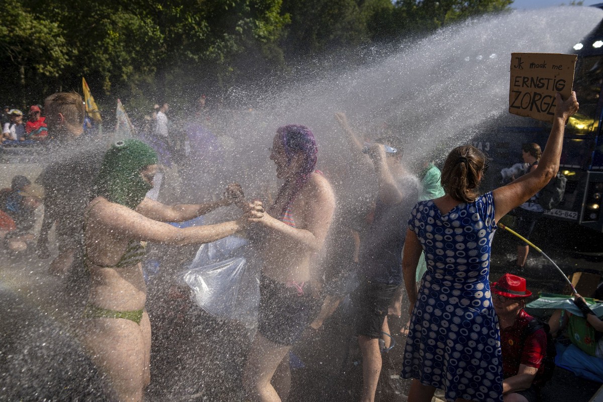 09.09.2023, Niederlande, Den Haag: Klimaaktivistinnen tanzen im Wasserstrahl eines Wasserwerfers der niederländischen Polizei während einer Klimaprotestaktion von Extinction Rebellion und anderen Akti ...