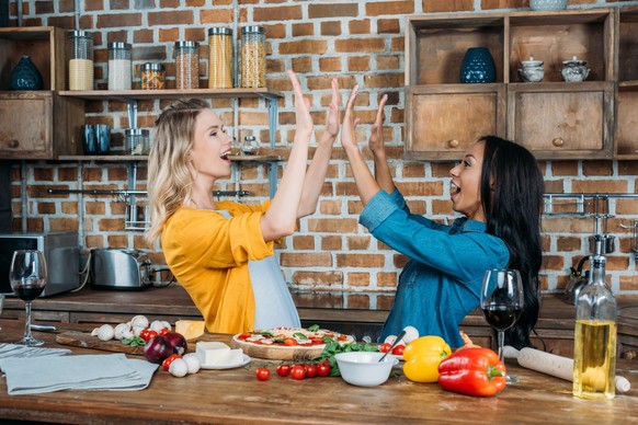 Cheerful young miltiehnic women giving high five while cooking in kitchen