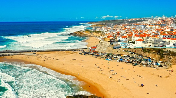 Drone view to Beautiful resort touristic town on ocean background. Aerial view - Beautiful travel destination with sandy beach. Tourist beach for surfing while vacation at Ericeira, in Summer.