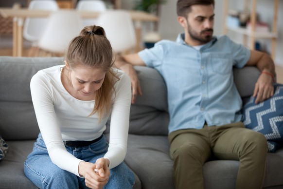 Unhappy young millennial married couple sitting on couch in living room after quarrel fight. Angry husband frustrated offended wife at home. Break up, divorce and misunderstanding in relations concept