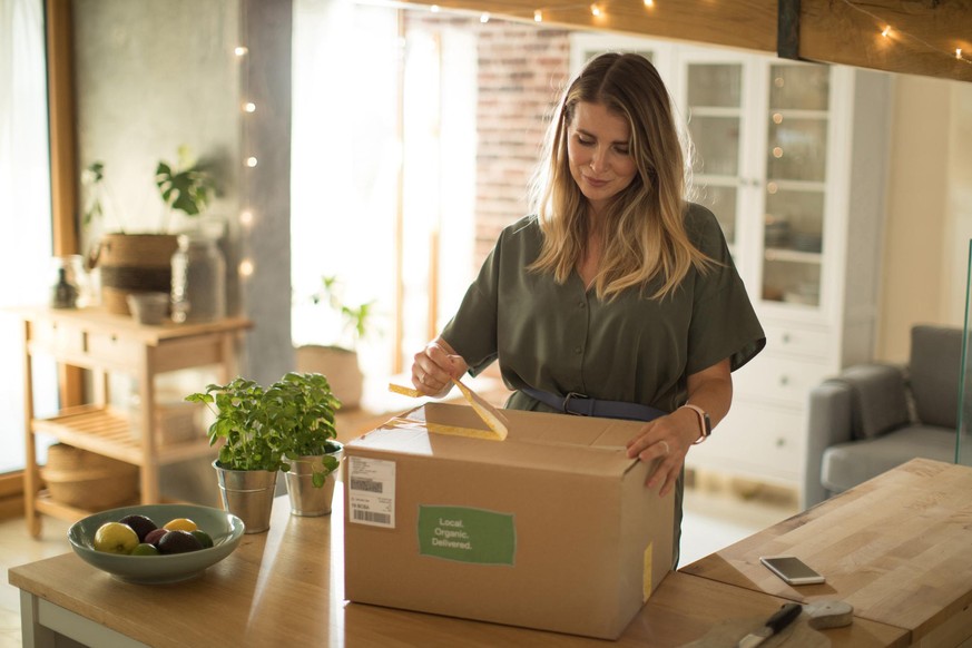 Woman is received box loaded with organic vegetables from delivery service. She is up to make some fantastic vegan meal