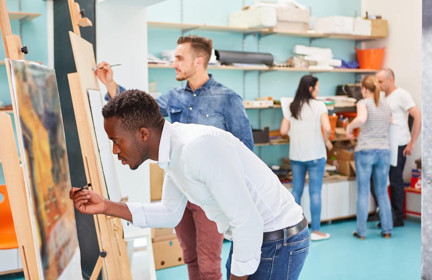 Junge Kunststudenten malen zusammen auf Leinwand an der Staffelei im Kunstkurs