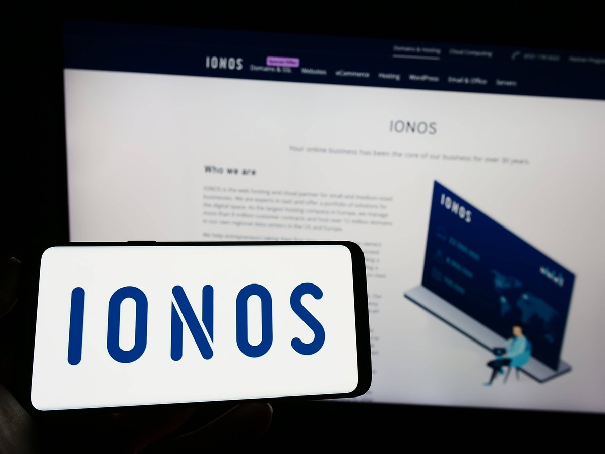 Person holding cellphone with logo of German web hosting company Ionos SE on screen. Stuttgart, Germany - 01-21-2023: Person holding cellphone with logo of German web hosting company Ionos SE on scree ...