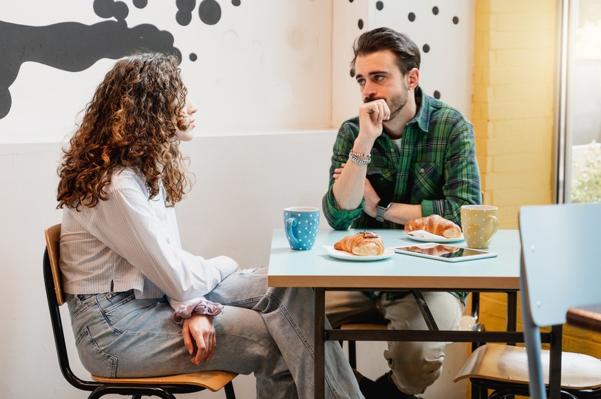 Young couple sitting at table in a cafe talking with serious faces.