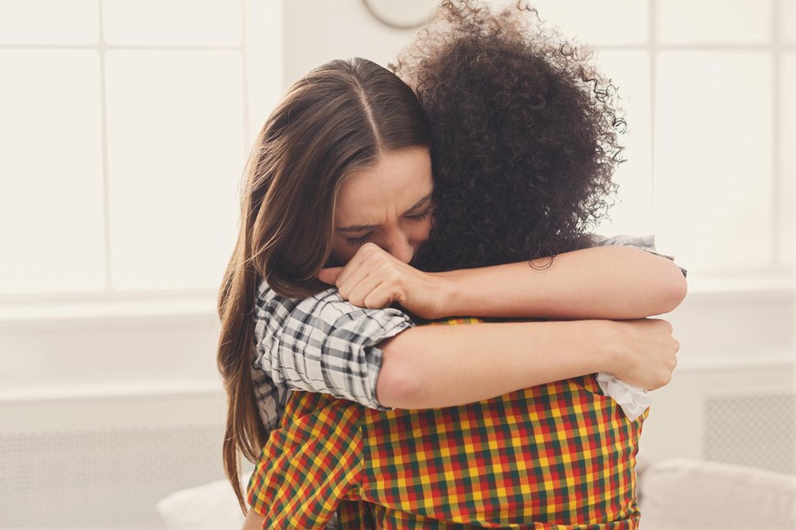 Woman hugging her depressed friend at home, closeup. Young girl supporting her crying girlfriend. Friendship consoling and care, copy space