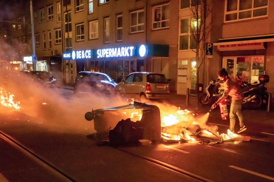 January 25, 2021, The Hague, Netherlands: Local resident attempts to extinguish fire started by the rioters..Riot police and Caine units gathered in mass, prior to the 9 o clock curfew as rioters and  ...