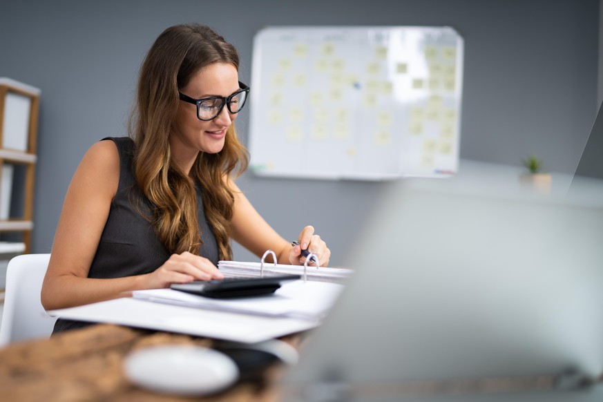 Portrait Of Smiling Businesswoman Calculating Tax At Desk In Office