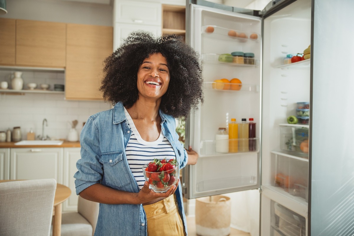 oman taking food from fridge full of groceries.