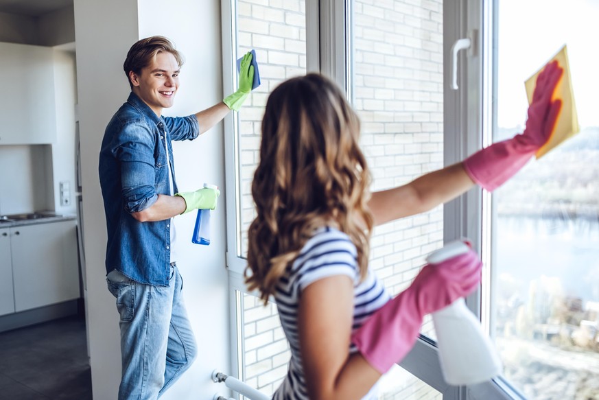 Young happy couple is washing windows while doing cleaning at home.