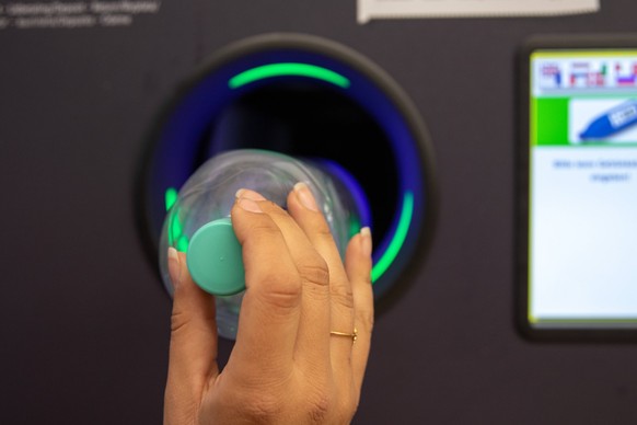 Una joven arroja botellas de plástico vacías a una máquina expendedora.  Devolución automatizada de envases vacíos Una joven arroja botellas retornables a la máquina expendedora *** Una joven arroja botellas de plástico retornables vacías a la máquina automatizada...