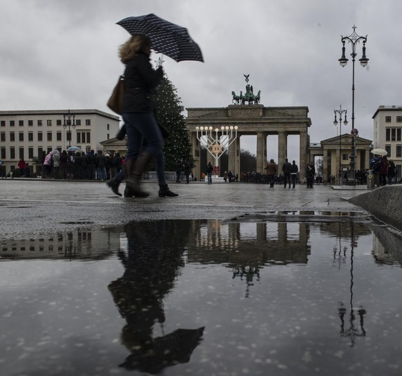 Eine Fußgängerin mit Regenschirm und das Brandenburger Tor spiegeln sich am 23.12.2014 in Berlin in einer Regenpfütze. Das Wetter ist am Dienstag für die Jahreszeit zu warm, windig und regnerisch. Ein ...