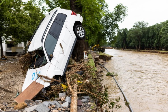 Ein vom Hochwasser angeschwemmtes Auto lehnt an einem Baum während im Hintergrund der Fluss Ahr zu sehen ist.