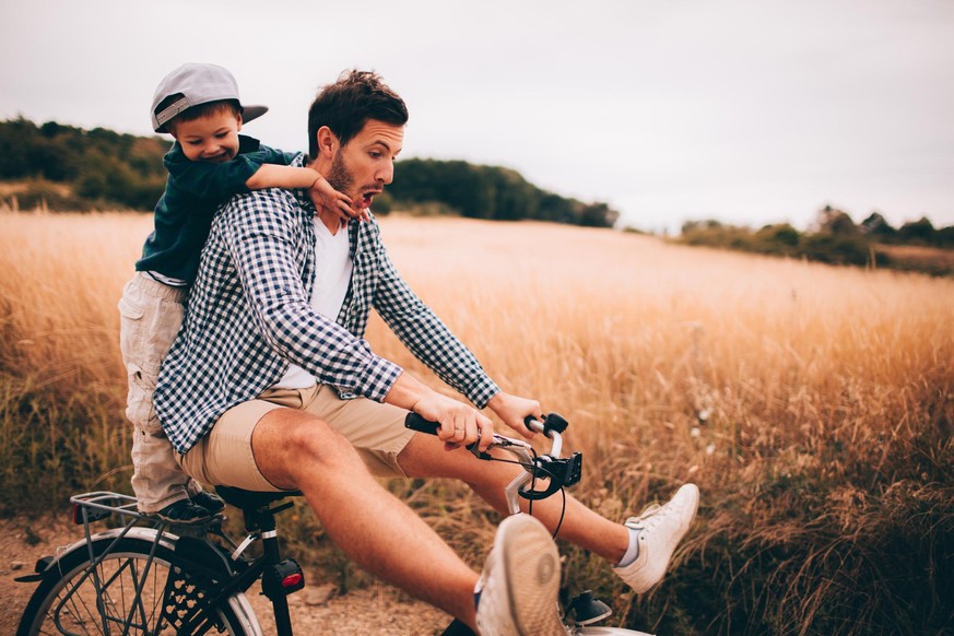Little boy and his father are riding a bicycle outdoors in the nature