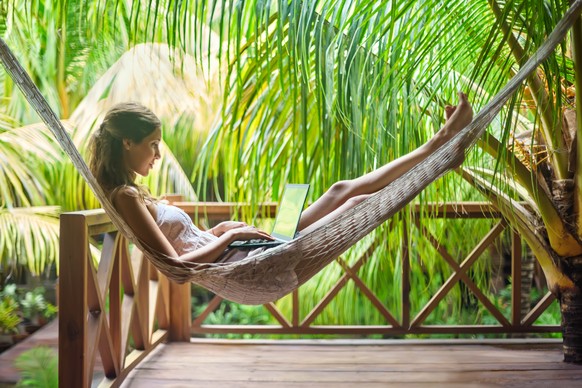 Young beautiful woman lying in a hammock with laptop in a tropical resort