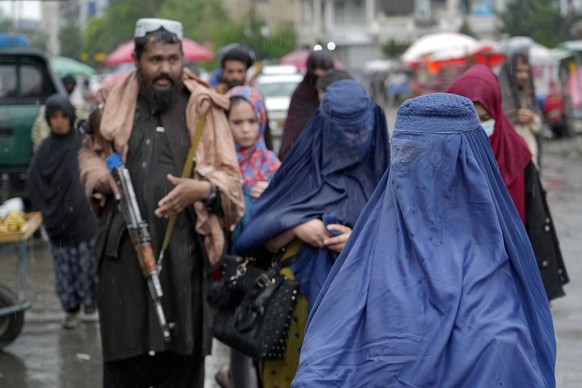 dpatopbilder - 03.05.2022, Afghanistan, Kabul: Frauen gehen durch den alten Markt, w�hrend im Hintergrund ein bewaffneter Taliban-K�mpfer Wache steht. Innerhalb weniger Tage sind in Afghanistan landes ...