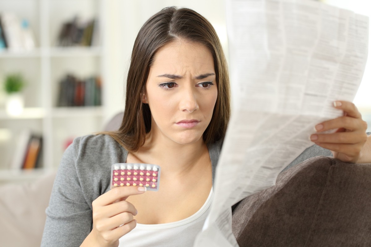 Worried woman reading contraceptive pills leaflet sitting on a couch at home