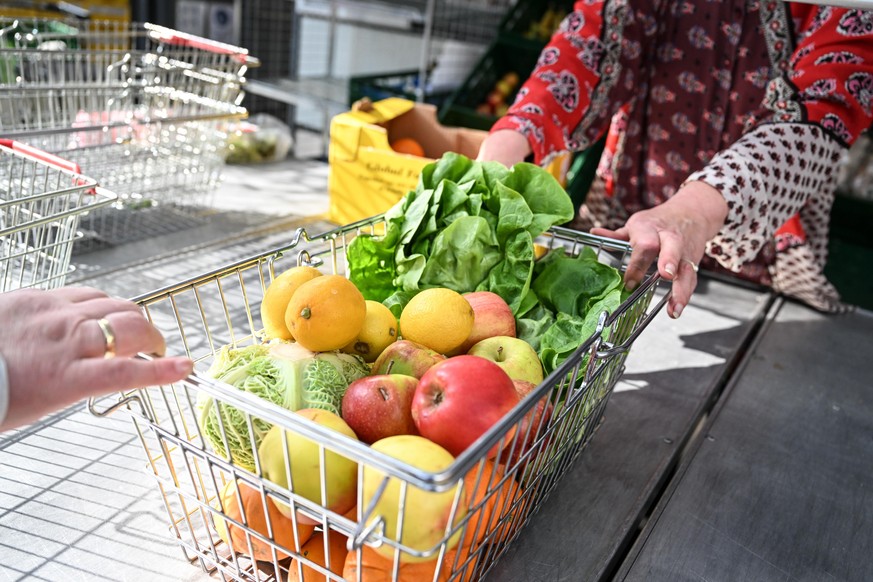 Eine Mitarbeiterin des Tafel-Ladens schiebt einen mit Obst und Gemüse gefüllten Einkaufskorb über den Tisch zu einer bedürftigen Frau, die diese Lebensmittel gerade zu einem günstigen Preis eingekauft ...