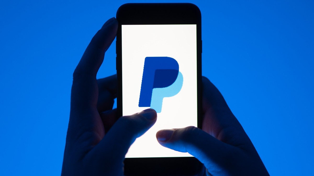 ARCHIV - 12.05.2022, Sachsen, Dresden: ILLUSTRATION - Eine Frau hält ein Smartphone mit dem Logo des Bezahldienst Paypal. (gestellte Szene) Der Online-Bezahldienst Paypal will angesichts des schwierig ...