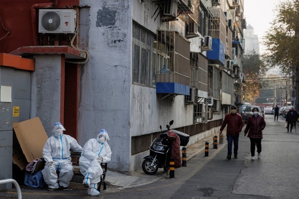 Epidemic prevention workers in protective suits sit in a locked-down residential compound as outbreaks of the coronavirus disease (COVID-19) continue in Beijing, November 23, 2022. REUTERS/Thomas Pete ...