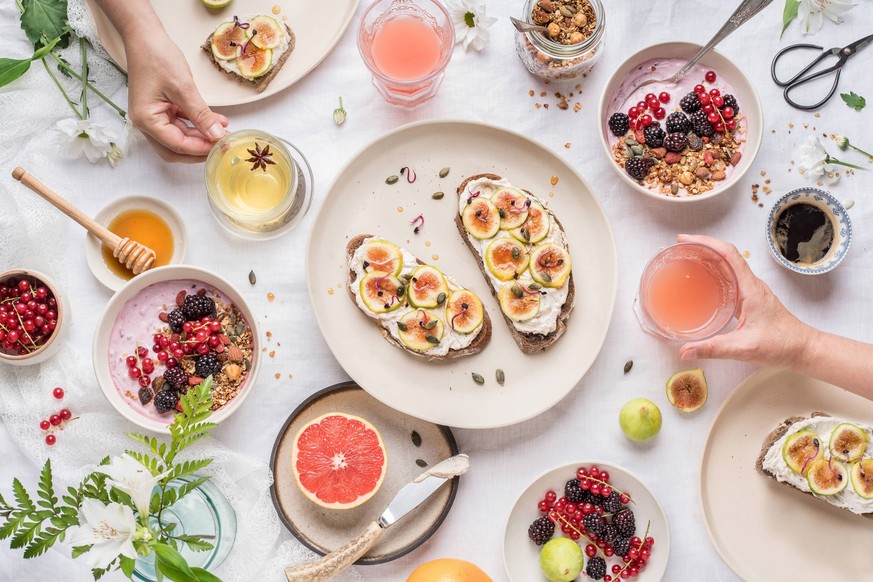 From above anonymous people taking cups of fresh healthy beverages from table with assorted food for breakfast Copyright: xAnaxGomezx