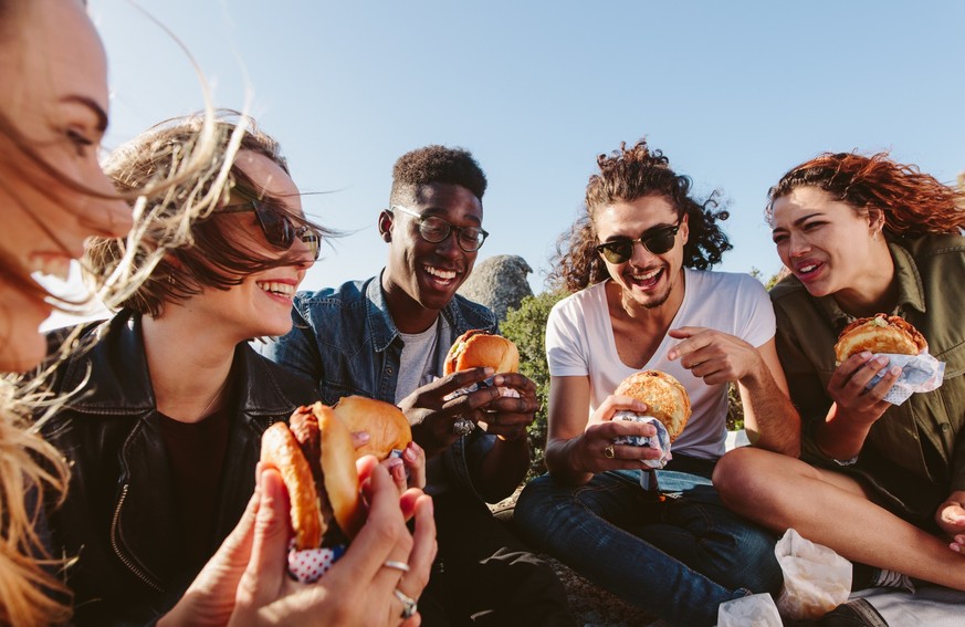 Young people having summer picnic and eating together sitting on mountain top. Happy friends on mountain top having a picnic on a summer day.