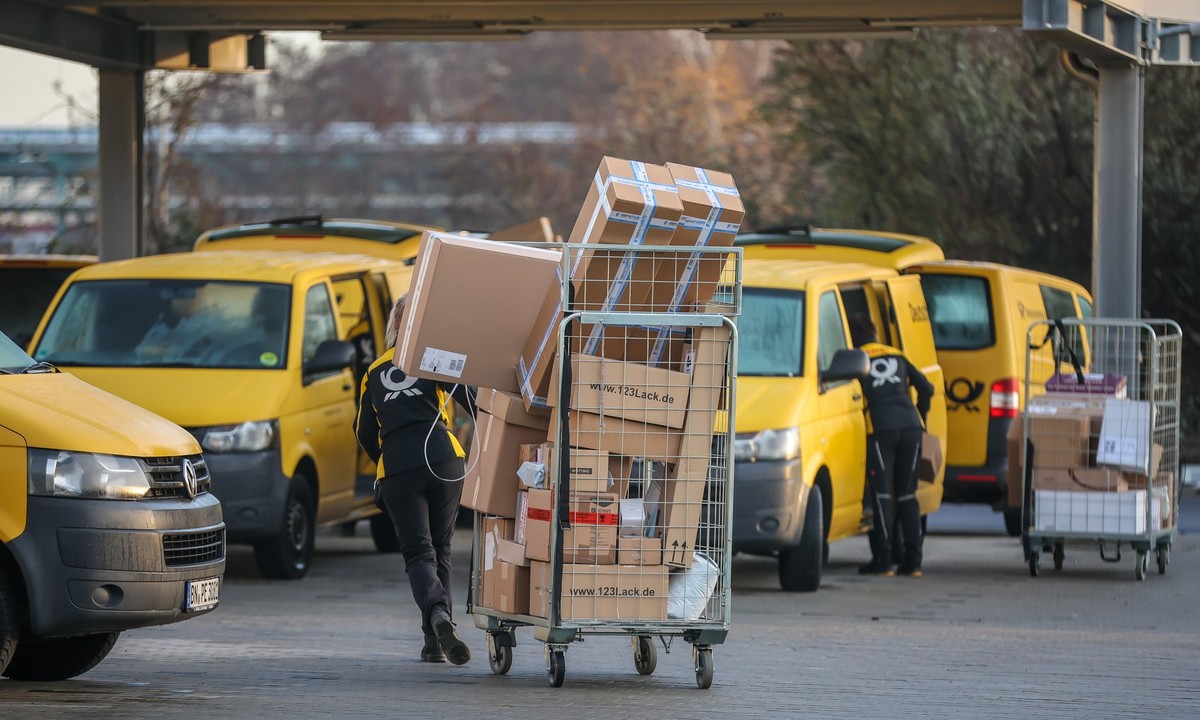 ARCHIV - 25.11.2022, Sachsen-Anhalt, Bitterfeld-Wolfen: Eine Mitarbeiterin der Deutsche Post DHL zieht einen vollen Paketwagen zu ihren Fahrzeug über den Hof eines Zustellpunktes. (zu dpa: «Die Post b ...