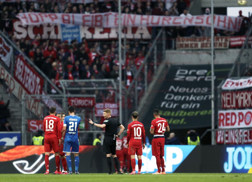 Referee Christian Dingert, center, talks to Hoffenheim and Munich players while Munich fans on the tribune display a banner reading &quot;Hopp stays a son of a bitch&quot; during a German Bundesliga s ...