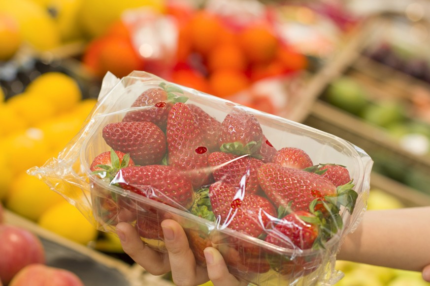 Female hand choosing strawberries in the store. Concept of healthy food, bio, vegetarian, diet.