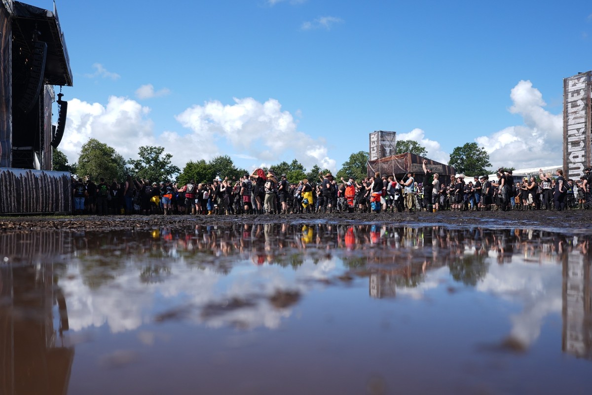 31.07.2025, Schleswig-Holstein, Wacken: Metal-Fans stehen vor einer Bühne auf dem matschigen Festivalgelände des Wacken Open Airs. Das Wacken Open Air (WOA) findet vom 30. Juli bis 2. August statt und ...