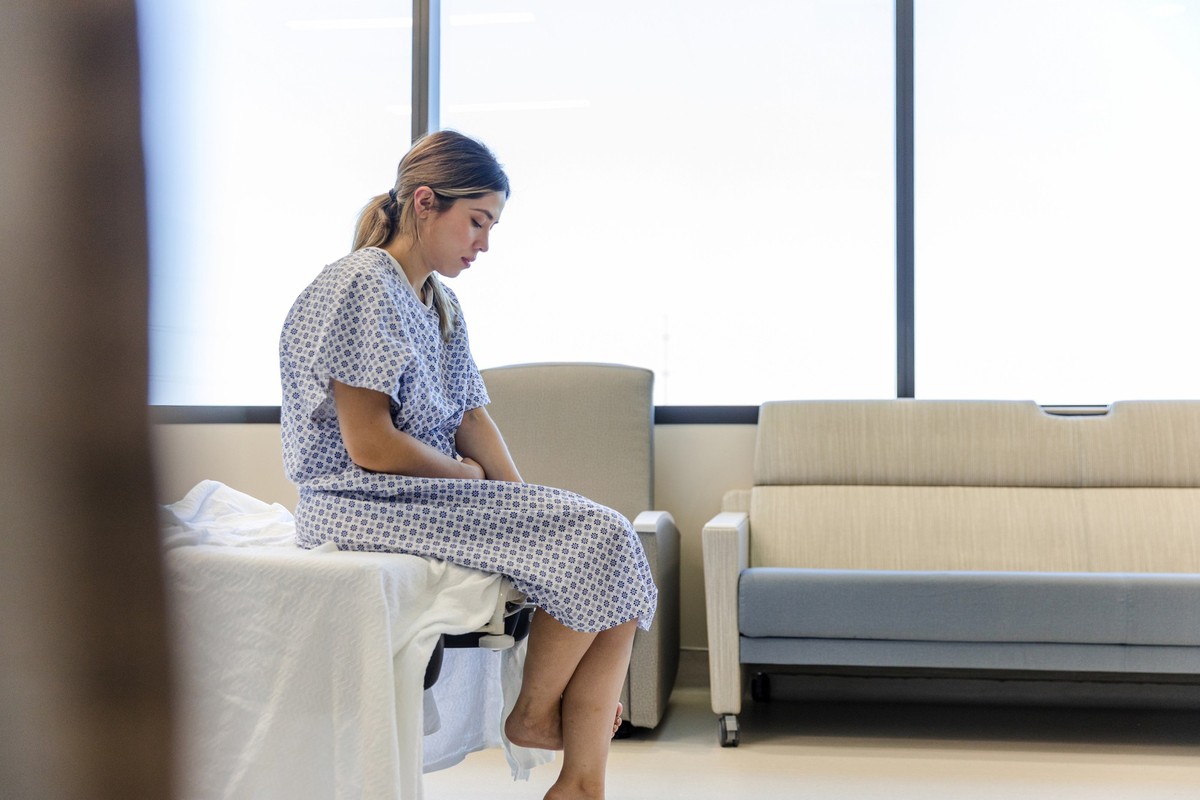The anxious, sad, young female patient wears her gown as she waits in the hospital room. schwangerschaft fehlgeburt totgeburt stille geburt pregnant sternenmama