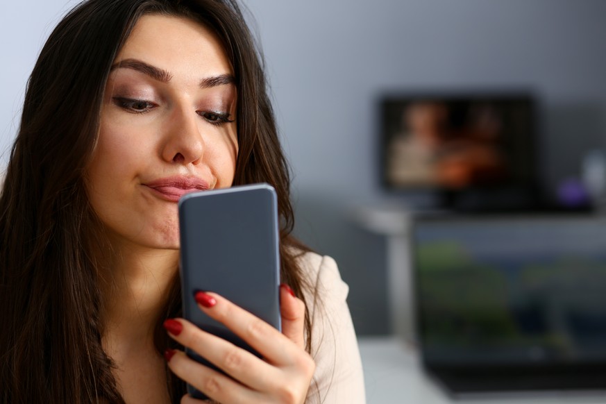 Young beautiful businesswoman unhappily holding smartphone in her hand contemptuously looks at display