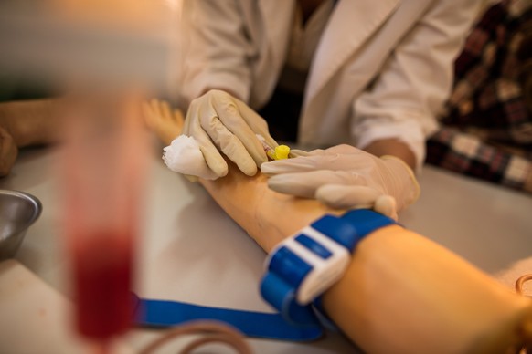 Unrecognizable doctor taking blood sample from artificial hand.