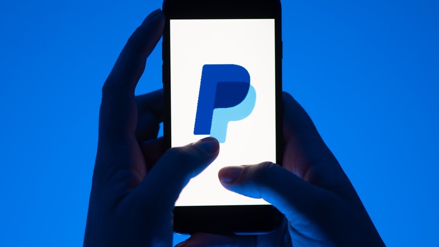 ARCHIV - 12.05.2022, Sachsen, Dresden: ILLUSTRATION - Eine Frau hält ein Smartphone mit dem Logo des Bezahldienst Paypal. (gestellte Szene) Paypal gibt am 03.11.2022 Zahlen für das 3. Quartal bekannt. ...