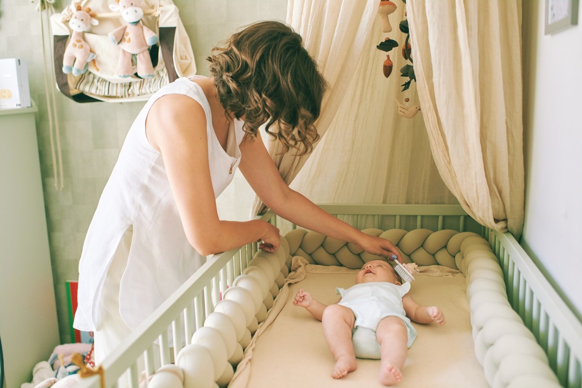 Young mother taking care of her little baby, child lying in a crib
